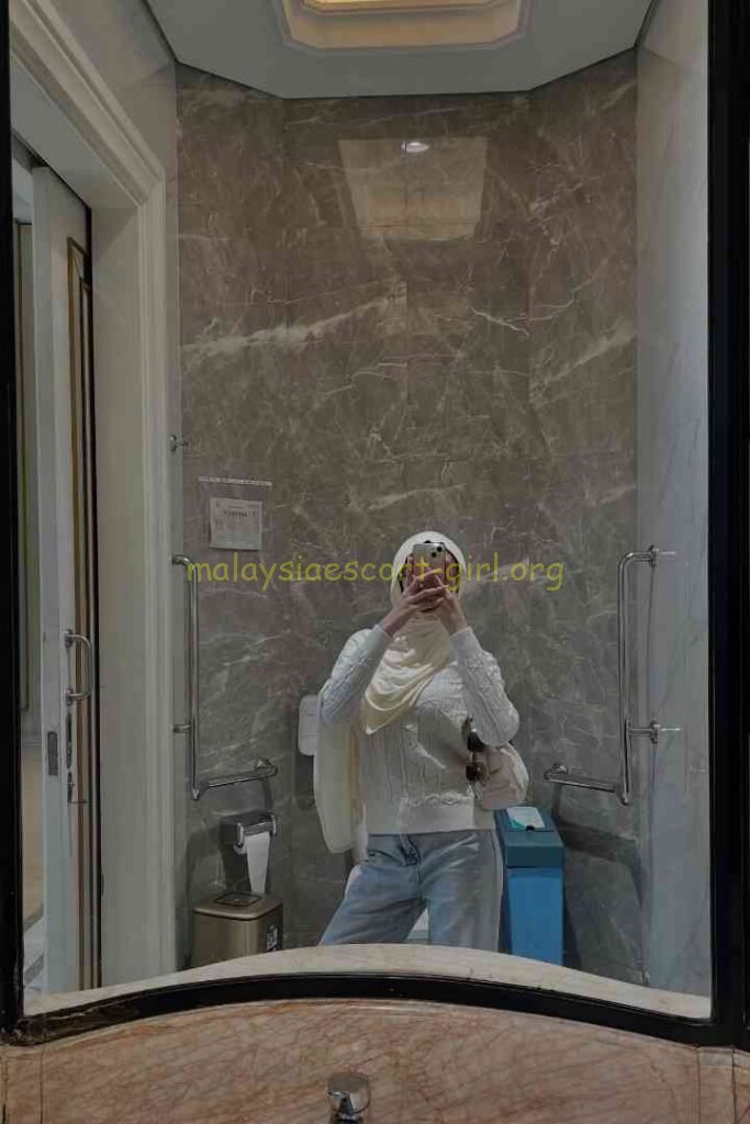 Woman taking selfie in bathroom with marble walls and white porcelain fixtures