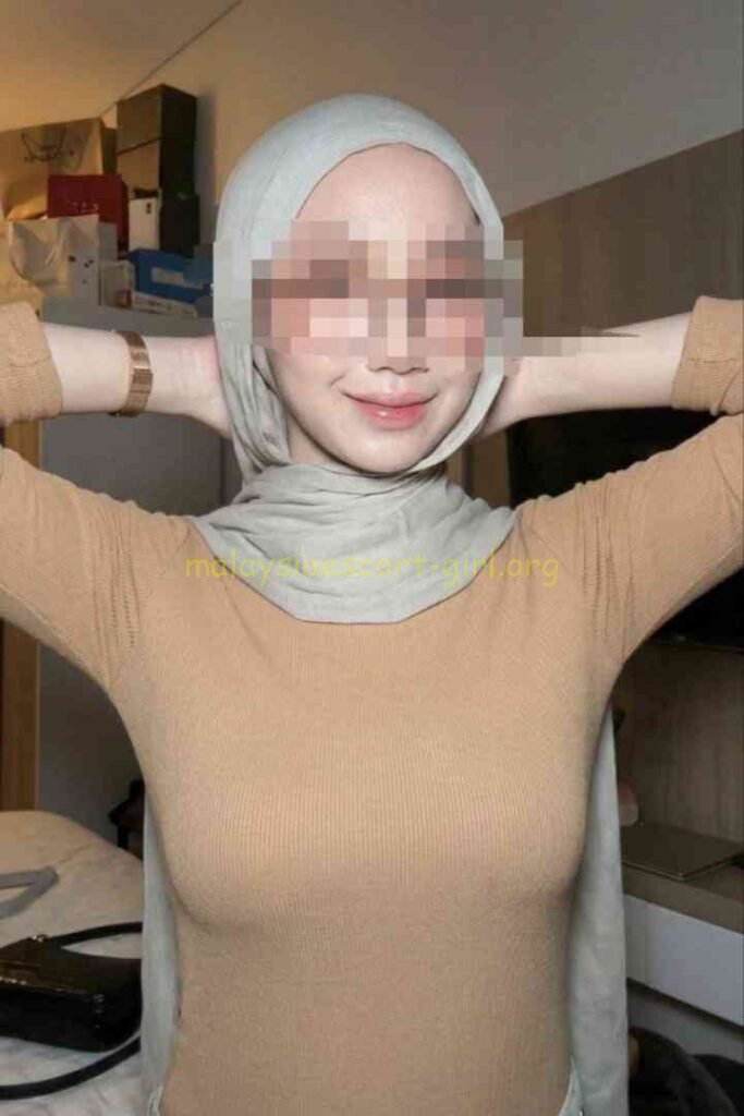 Malaysia Escort posing in a room with blurred background, wearing a hijab